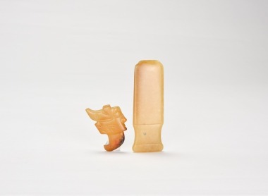 A Group of Two Jade Ornaments: A Human-Deity Pendant and a Handle-Shaped Implement. Shang Dynasty, ca. 16th&ndash;11th century BC. (1) Human-Deity Pendant. Carved from yellowish-brown jade. (2) Handle-Shaped Jade Implement.